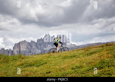 Cortina d'Ampezzo, Italien - 18. August 2018: Ein solo Radfahrer pedal bergauf auf dem Berg weg, an einem bewölkten Sommertag. Im Hintergrund der Gipfel des Stockfoto