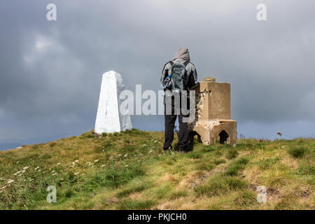 Wanderer mit Rucksack, Haube, Ladekabel und Wasserflasche stehen in der Nähe des Gipfels Steine Stockfoto