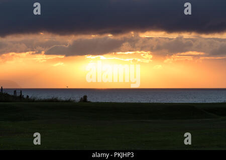 Dramatische orange Sonnenuntergang durch dunkle Wolken über der Nord Antrim Coast, Portstewart, N. Irland zu brechen. Stockfoto