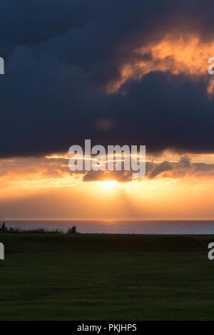 Dramatische orange Sonnenuntergang durch dunkle Wolken über der Nord Antrim Coast, Portstewart, N. Irland zu brechen. (Vertikal) Stockfoto