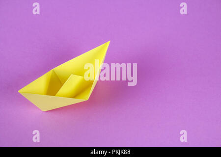 Gelbes Papier Boot von Origami mit einem Herbst Blatt auf einem violetten Hintergrund Stockfoto