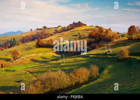 Leere Heu Kasernen auf einem grasbewachsenen Hügel inmitten von Bäumen in rot Laub. wunderschöne Herbstlandschaft, die in der fernen Tal. ländlichen Lebensstil Stockfoto