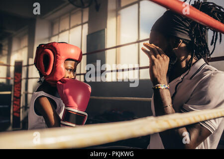 Boxtrainer erteilen Anweisungen an ein Kind zu einem Boxing Gym. Kid Boxhandschuh und Kopfbedeckungen Training mit seinem Trainer in einem Boxring. Stockfoto