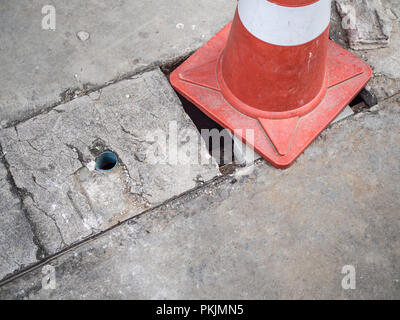 Orange Leitkegel Kunststoff Straße auf der Grunge defekt Zement Abdeckung der Ablassen warten auf die Reparatur mit kopieren. Stockfoto
