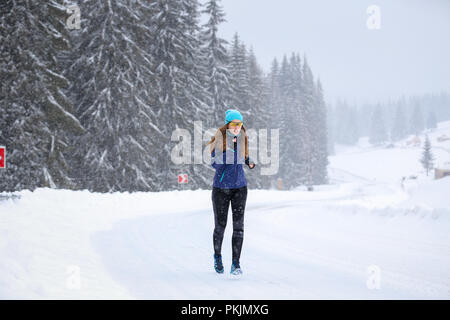 Junge Frau, die auf dem Berg Straße im Winter Stockfoto