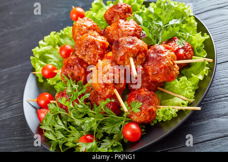 Close-up auf Fleischbällchen am Spieß mit frischen Tomaten auf einem Bett von Grüns auf einer schwarzen Platte, Street Food, horizontale Ansicht von oben Stockfoto