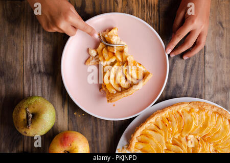 Kleines Mädchen Hände essen einen Teil der Apfelkuchen Torte auf einem rosa Teller auf rustikalen Holzmöbeln Hintergrund. Ansicht von oben Stockfoto