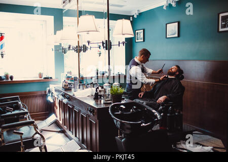 Barbershop mit Interieur aus Holz. Bärtige Modell Mann und Friseur. Stockfoto