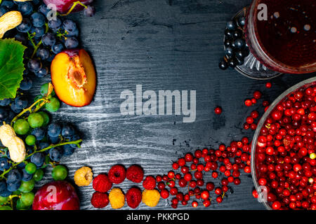 Lebensmittel, die reich an Resveratrol, Trauben, Pflaumen, Goji, Erdnüsse, Cranberry, raspberrys dunkle Schokolade, Rotwein auf schwarzem Holz- Hintergrund Stockfoto
