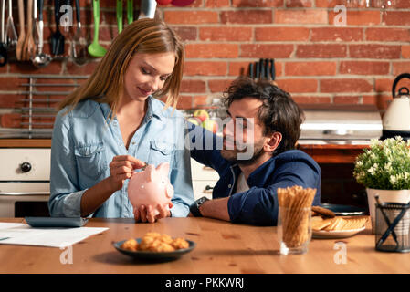 Familie, Haushalt und Finanzen. Junge Frau setzt eine Münze in das Sparschwein. Stockfoto