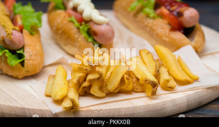 Knusprige golden Pommes frites auf einem Holzbrett serviert mit sortierten Baguettes mit gegrillten Würstchen und Garnituren Stockfoto