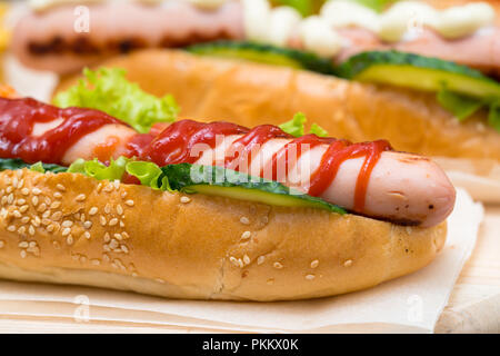 Hot Dog beträufelt mit Tomatenketchup und mit frischen Gurken und Salat serviert auf einem frischen Sesam roll in der Nähe zu sehen. Stockfoto