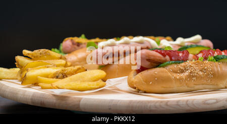 Sortierte Spezialität hot dogs mit verschiedenen Seite Garnituren und Dressings mit frittierten Kartoffelchips auf einem Holzbrett in Banner Format serviert. Stockfoto