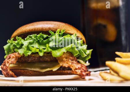 Lecker käse und bacon Burger mit Pommes frites auf einem rustikalen Holzbrett serviert gesehen niedrigen Winkel Stockfoto