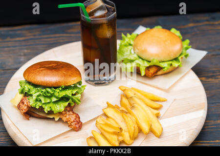 Doppelte Umhüllung von zwei Burger mit Pommes Frites und ein hohes Glas von Soda oder Cola mit Eis auf einem runden Holzbrett gesehen hohen Winkel Stockfoto