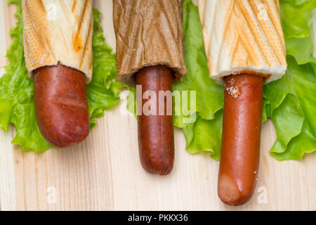 Über dem Kopf Blick auf drei Brötchen Brot gefüllt mit Hot Dogs mit unterschiedlicher Länge auf Salat sitzen Stockfoto