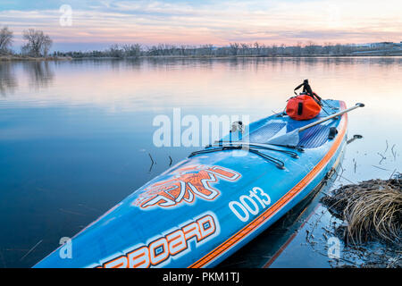 Fort Collins, CO, USA - 11. März 2018: Stand up paddleboard von Steuerbord mit einem wasserdichten Duffle und ein Paddel auf einem ruhigen See nach Sonnenuntergang. Stockfoto