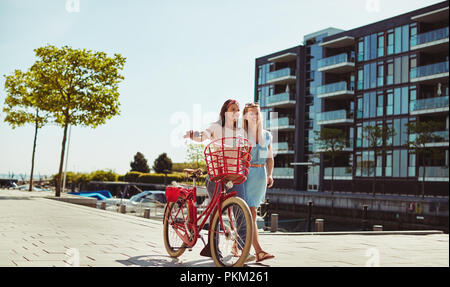 Zwei Freundinnen lachen und Spaß haben, während der gemeinsame Weg mit dem Fahrrad durch die Stadt im Sommer Stockfoto