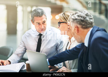 Drei ältere Führungskräfte sitzen an einem Schreibtisch diskutieren Schreibarbeit und über einen Laptop während einer Sitzung gemeinsam in einem Büro Stockfoto
