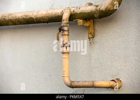 Close-up Detail des Alten schmutzig gelb lackiert Erdgasleitungen mit Schweißnähte und Hahn Ventil befestigt, um graue Hauswand. Sicherheit, Gefahr, alt und Stockfoto