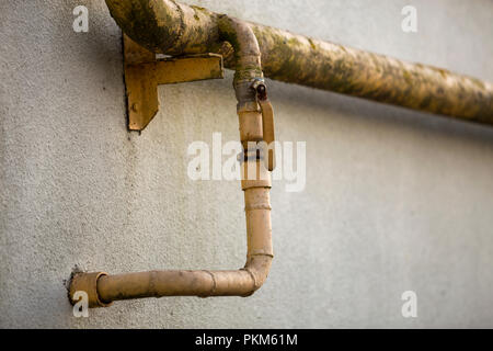 Close-up Detail des Alten schmutzig gelb lackiert Erdgasleitungen mit Schweißnähte und Hahn Ventil befestigt, um graue Hauswand. Sicherheit, Gefahr, alt und Stockfoto