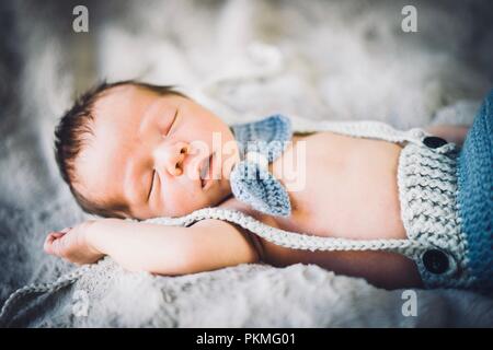 Ein neugeborenes Baby schlafen in Blau und Grau aus Gewirken Bow Tie und Hose, Portugal Stockfoto