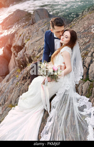 Schönes Paar in Liebe küssen, während er auf den Felsen in der Nähe des Flusses. Hochzeit paar bei Sonnenuntergang und Flüsse, Liebe und zärtliche Gefühle. Paar r Stockfoto