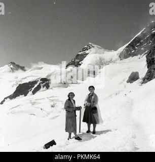 1950, historische, zwei Damen, im normalen täglichen cothes gekleidet, für einen Spaziergang auf den schneebedeckten Pisten der alpinen Ski Resort Arosa, Schweiz, Stockfoto