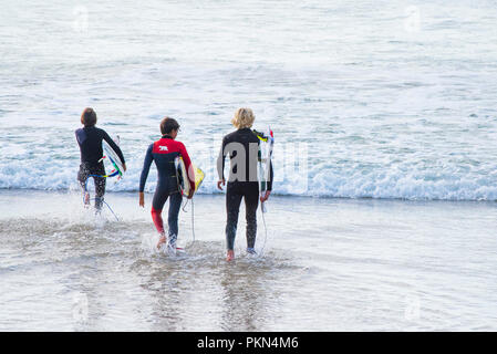 Drei junge Surfer ihre Surfbretter und Betrieb in das Meer bei Fistral Beach in Newquay Cornwall. Stockfoto