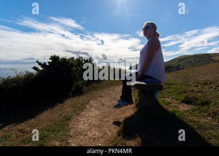 Frau auf einer Bank sitzen an der Spitze der Klippen auf das Meer schauen und durch helles Sonnenlicht. Stockfoto