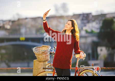 Eine schöne junge Frau mit einem retro rot Fahrrad macht ein Foto von sich in der alten Stadt Europas am Rhein Damm in der Schweizer cit Stockfoto