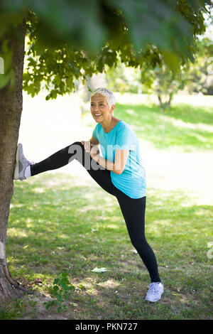 Ältere Frau sich ausdehnende Übung im Park von Baum Stockfoto