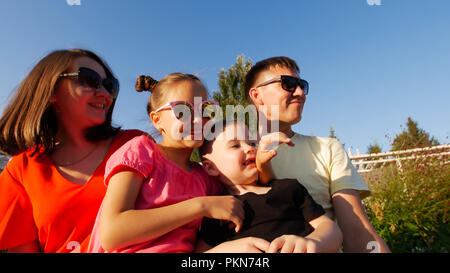 Junge, glückliche Familie im Park sitzen an einem sonnigen Sommertag, tragen Sonnenbrillen Stockfoto