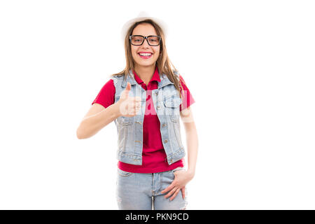 Sehr trendy Frau in Jeans und Hut mit Daumen hoch auf weißer Wand lächelt Kamera isoliert Stockfoto