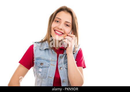 Junge Teenager Frau in Denim Weste lächelnd an der Kamera und am Telefon sprechen auf weißem Hintergrund Stockfoto