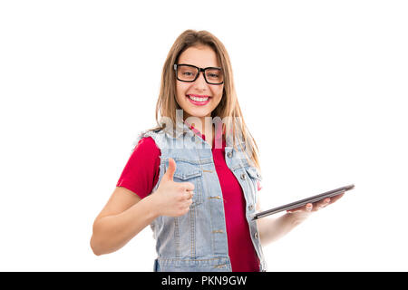 Junge moderne Frau in Jeans Weste und Brillen holding Tablet und zeigt mit dem Daumen oben auf weißem Hintergrund Stockfoto