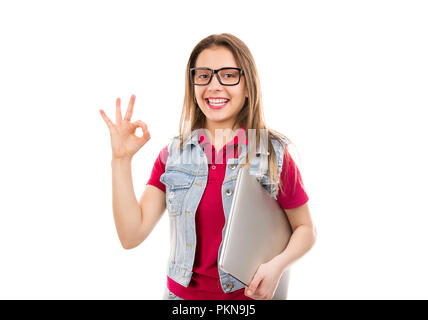 Hübsche junge Frau in Jeans mit Laptop und mit OK Geste lächeln auf die Kamera auf weißem Hintergrund Stockfoto