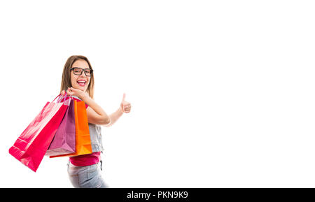Seitenansicht des stilvollen glücklich Frau in Gläser mit bunten Einkaufstaschen holding Daumen oben auf weißem Hintergrund Stockfoto