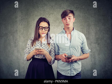 Junger Mann und Frau suchen und Spähen in der ungläubigkeit in Smartphones voneinander Stockfoto