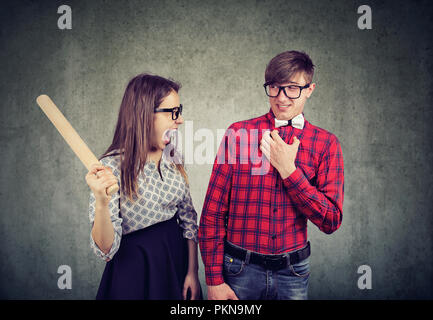 Junge Frau mit Rolling Pin suchen verrückt, während das Argumentieren mit Mann auf grauem Hintergrund Stockfoto
