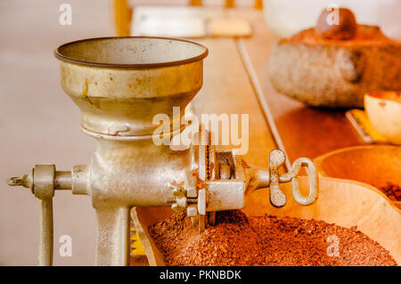 Nahaufnahme von Kakaobohnen und Kakao über einen hölzernen Tisch gefräst, mit Mühle, in einem verschwommenen Hintergrund Stockfoto