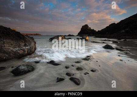 Ein Blick auf den Sandstrand und die Wellen über Felsen an Kynance Cove in Cornwall, UK hetzen Stockfoto