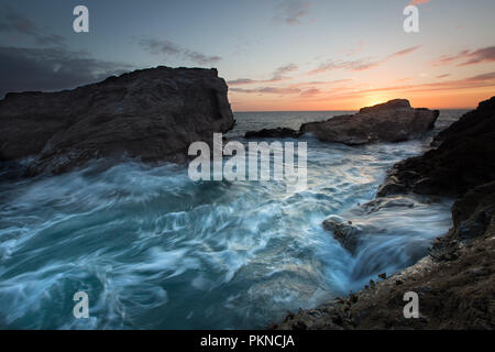 Eine zerklüftete Küsten Sonnenuntergang Bild der Wellen über rauen Felsen mit Motion Blur Auf der Cornwall in Cornwall, UK fließt. Stockfoto
