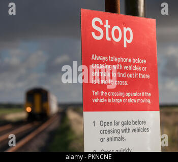 Ein Zug nähert sich einem umzäunten Benutzer arbeitete Bahnübergang mit der STOP-Schild- und Bedienungsanleitung auf der Cumbrian Küste bei Dunnerholme Stockfoto