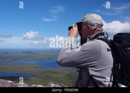 Mann in der 60er Jahre durch ein Fernglas trägt eine Kappe und Rucksack von Stac Pollaidh über inverpolly Wald auf einem hellen, sonnigen Tag im Alter von Stockfoto