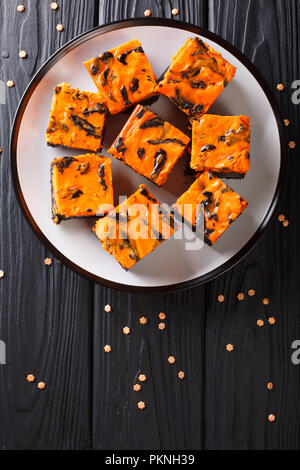 Halloween Essen Dark Chocolate Brownie mit einer Schicht von Orangen Käsekuchen Nahaufnahme auf die Platte auf einem Tisch lagen. Vertikal oben Ansicht von oben Stockfoto