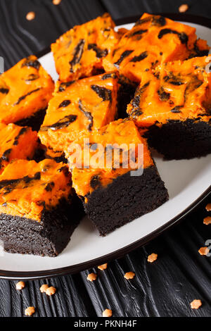 Halloween dessert Cream Cheese Brownies, bestehend aus einer dunklen Schokolade Kuchen gekrönt mit einer Schicht von Orangen Käsekuchen close-up auf einem Teller. Vertikale Stockfoto