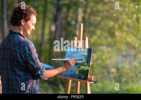 Junge hübsche Frau Künstler zeichnet, malt ein Bild von einem See auf dem offenen plain air im Freien Stockfoto