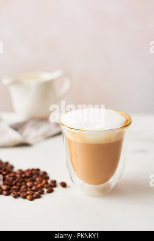 Cappuccino in einem doppelwandigen Glas mit gerösteten Kaffeebohnen. Feminine rose Hintergrund mit kopieren. Bild mit hoher Auflösung, enge Tiefenschärfe. Stockfoto