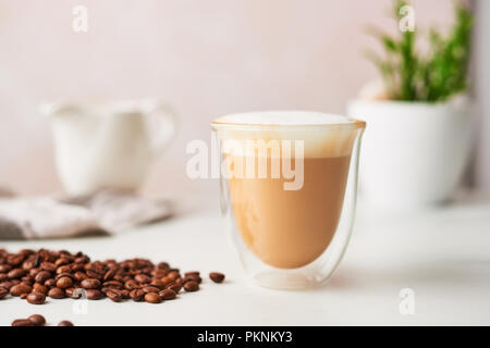 Cappuccino in einem doppelwandigen Glas mit gerösteten Kaffeebohnen. Feminine rose Hintergrund mit kopieren. Bild mit hoher Auflösung, enge Tiefenschärfe. Stockfoto